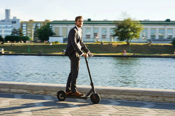 Joven hombre de negocios en un traje montando un scooter eléctrico en una reunión de negocios. —  Fotos de Stock