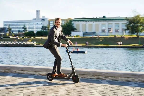 Joven hombre de negocios en un traje montando un scooter eléctrico en una reunión de negocios. —  Fotos de Stock