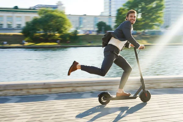 Joven hombre de negocios en un traje montando un scooter eléctrico en una reunión de negocios. —  Fotos de Stock