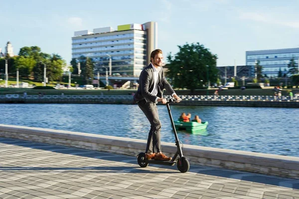 Joven hombre de negocios en un traje montando un scooter eléctrico en una reunión de negocios. —  Fotos de Stock