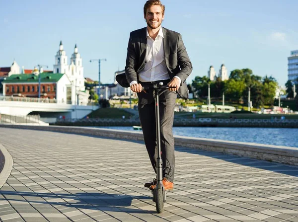 Jovem homem de negócios em um terno montando uma scooter elétrica em uma reunião de negócios. — Fotografia de Stock