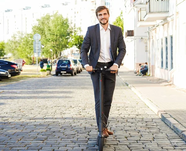 Joven hombre de negocios en un traje montando un scooter eléctrico en una reunión de negocios. —  Fotos de Stock