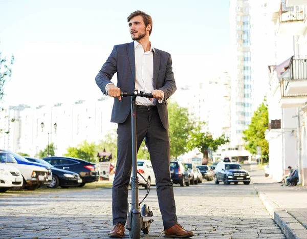Joven hombre de negocios en un traje montando un scooter eléctrico en una reunión de negocios. —  Fotos de Stock