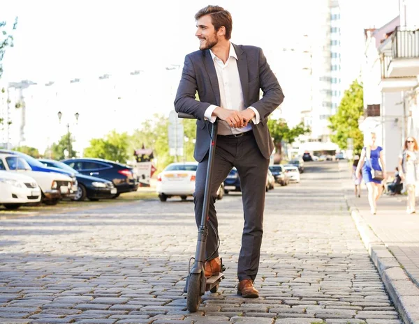 Joven hombre de negocios en un traje montando un scooter eléctrico en una reunión de negocios. —  Fotos de Stock