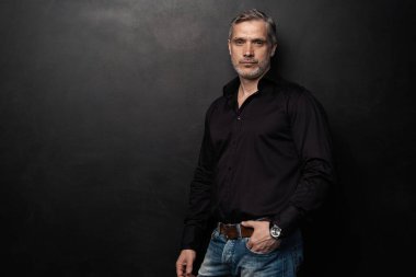 Orta yaşlı yakışıklı bir adam siyah bir arkaplan önünde fotokopi alanı ile poz veriyor..