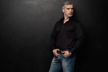 Orta yaşlı yakışıklı bir adam siyah bir arkaplan önünde fotokopi alanı ile poz veriyor..