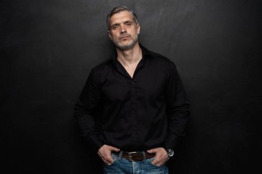 Orta yaşlı yakışıklı bir adam siyah bir arkaplan önünde fotokopi alanı ile poz veriyor..