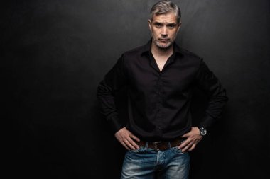 Orta yaşlı yakışıklı bir adam siyah bir arkaplan önünde fotokopi alanı ile poz veriyor..