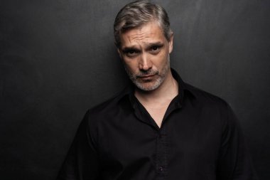 Orta yaşlı yakışıklı bir adam siyah bir arkaplan önünde fotokopi alanı ile poz veriyor..