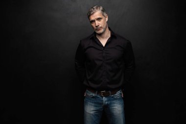 Orta yaşlı yakışıklı bir adam siyah bir arkaplan önünde fotokopi alanı ile poz veriyor..