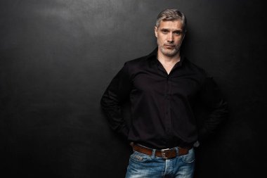 Orta yaşlı yakışıklı bir adam siyah bir arkaplan önünde fotokopi alanı ile poz veriyor..