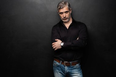 Orta yaşlı yakışıklı bir adam siyah bir arkaplan önünde fotokopi alanı ile poz veriyor..