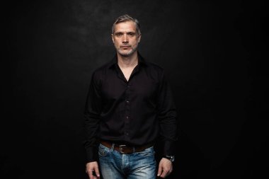 Orta yaşlı yakışıklı bir adam siyah bir arkaplan önünde fotokopi alanı ile poz veriyor..