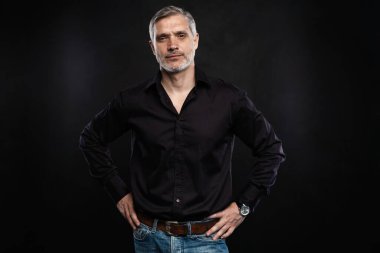 Orta yaşlı yakışıklı bir adam siyah bir arkaplan önünde fotokopi alanı ile poz veriyor..