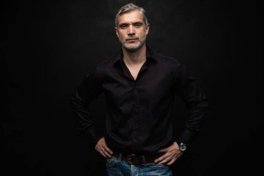 Orta yaşlı yakışıklı bir adam siyah bir arkaplan önünde fotokopi alanı ile poz veriyor..