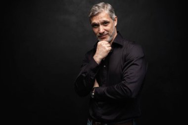 Orta yaşlı yakışıklı bir adam siyah bir arkaplan önünde fotokopi alanı ile poz veriyor..