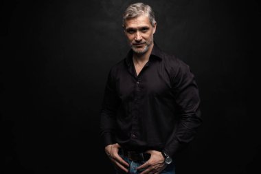 Orta yaşlı yakışıklı bir adam siyah bir arkaplan önünde fotokopi alanı ile poz veriyor..
