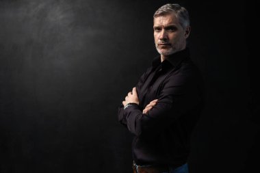 Orta yaşlı yakışıklı bir adam siyah bir arkaplan önünde fotokopi alanı ile poz veriyor..