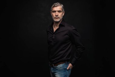 Orta yaşlı yakışıklı bir adam siyah bir arkaplan önünde fotokopi alanı ile poz veriyor..