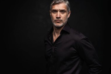 Orta yaşlı yakışıklı bir adam siyah bir arkaplan önünde fotokopi alanı ile poz veriyor..