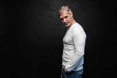 Beyaz tişörtlü orta yaşlı yakışıklı bir adam siyah arka planda fotokopi alanı ile poz veriyor..