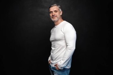 Beyaz tişörtlü orta yaşlı yakışıklı bir adam siyah arka planda fotokopi alanı ile poz veriyor..