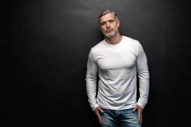 Beyaz tişörtlü orta yaşlı yakışıklı bir adam siyah arka planda fotokopi alanı ile poz veriyor..