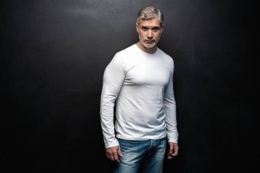 Beyaz tişörtlü orta yaşlı yakışıklı bir adam siyah arka planda fotokopi alanı ile poz veriyor..