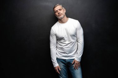 Beyaz tişörtlü orta yaşlı yakışıklı bir adam siyah arka planda fotokopi alanı ile poz veriyor..