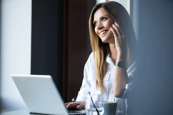 Heureuse femme d'affaires assise à la table et parlant au téléphone dans un café. En regardant ailleurs — Photo