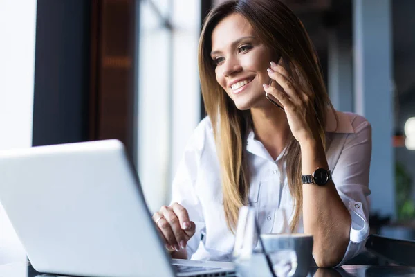 Heureuse femme d'affaires assise à la table et parlant au téléphone dans un café. En regardant ailleurs — Photo