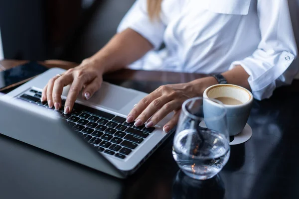Wanita muda yang cantik sibuk mengerjakan laptopnya duduk di meja di sebuah kedai kopi. — Stok Foto