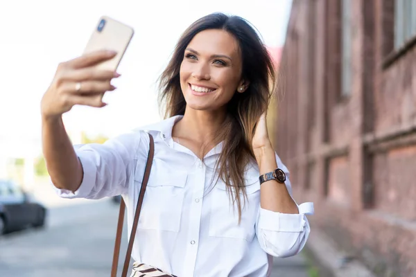 Şehirde yürürken telefonla selfie çeken güzel bir kadının açık hava yaşam tarzı portresi. — Stok fotoğraf