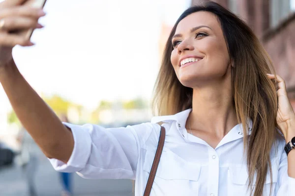 Şehirde yürürken telefonla selfie çeken güzel bir kadının açık hava yaşam tarzı portresi. — Stok fotoğraf