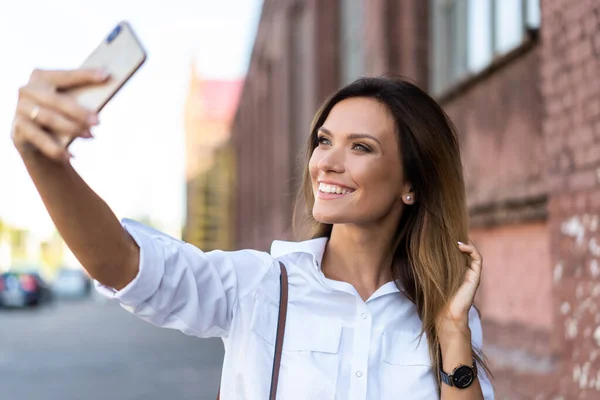 Şehirde yürürken telefonla selfie çeken güzel bir kadının açık hava yaşam tarzı portresi. — Stok fotoğraf