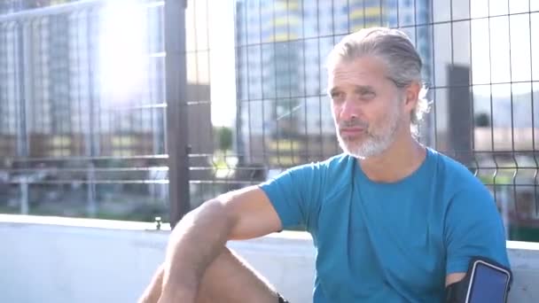 Homem moderno em sportswear fazer uma pausa após jogging ou exercício na área urbana — Vídeo de Stock