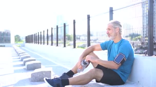 Homem moderno em sportswear fazer uma pausa após jogging ou exercício na área urbana — Vídeo de Stock