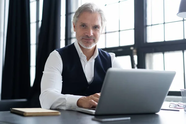 Geconcentreerd op het werk. Happy volwassen man in volle pak met behulp van laptop tijdens het werken in modern kantoor. — Stockfoto
