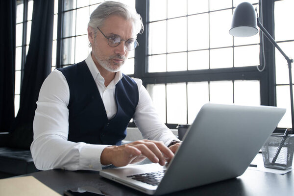 Concentrated at work. Mature man in full suit using laptop while working in modern office.