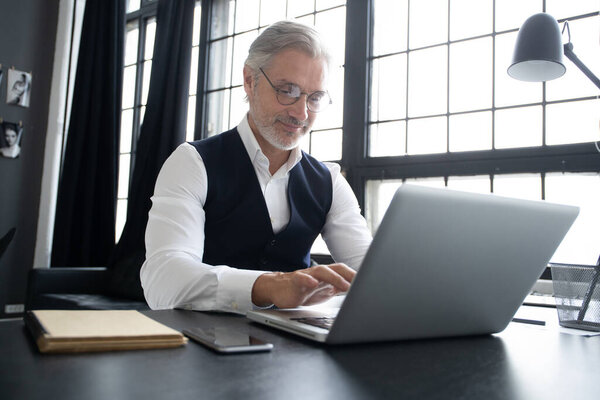 Concentrated at work. Mature man in full suit using laptop while working in modern office.