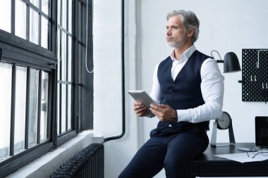 Yeni tablet üzerinde çalışıyorum. Ofisteki büyük pencerenin önünde dururken dijital tablet üzerinde çalışan kendinden emin bir adam..