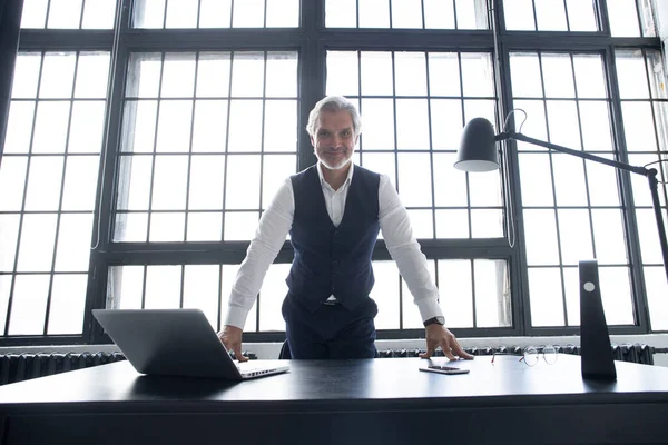 Zelfverzekerde zakenman poseert leunend op een tafel in een kantoor. — Stockfoto