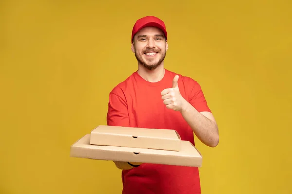 Glücklicher Mann vom Lieferdienst in rotem T-Shirt und Mütze, der Essen bestellt und Pizzakartons isoliert über gelb hält — Stockfoto