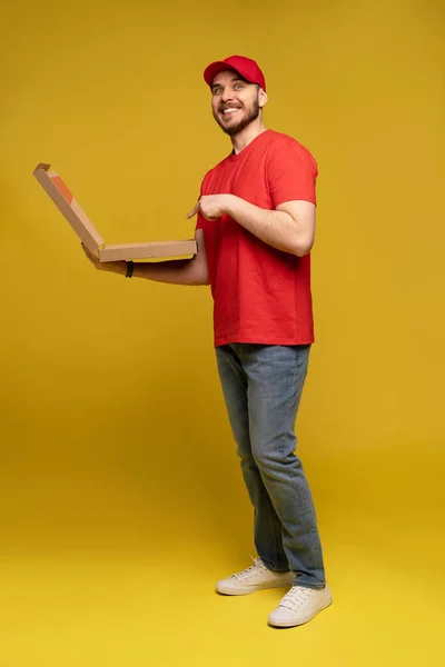 Homem feliz do serviço de entrega em t-shirt vermelha e tampa dando ordem alimentar e segurando caixa de pizza isolada sobre amarelo — Fotografia de Stock