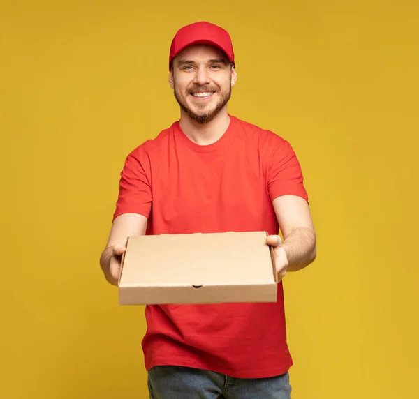 Hombre feliz del servicio de entrega en camiseta roja y gorra dando orden de comida y sosteniendo la caja de pizza aislada sobre amarillo — Foto de Stock
