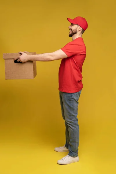 Delivery man with box in studio isolated on yellow background. — Stock Photo, Image