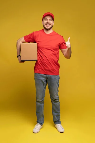 Delivery man with box in studio isolated on yellow background.