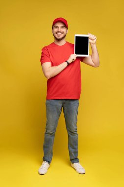 Stüdyoda tabletli mutlu teslimatçı sarı arka planda..