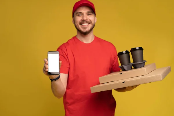 Junger Mann hält Pizza und Smartphone isoliert auf gelbem Grund. — Stockfoto