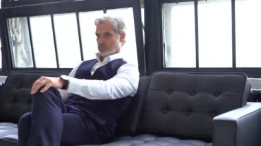 Kır saçlı zarif adam koltukta oturuyor..